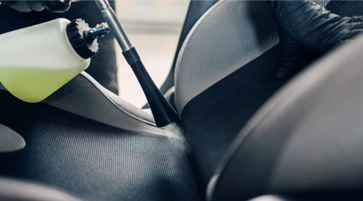 a man spraying car seat with a bottle of disinfectant