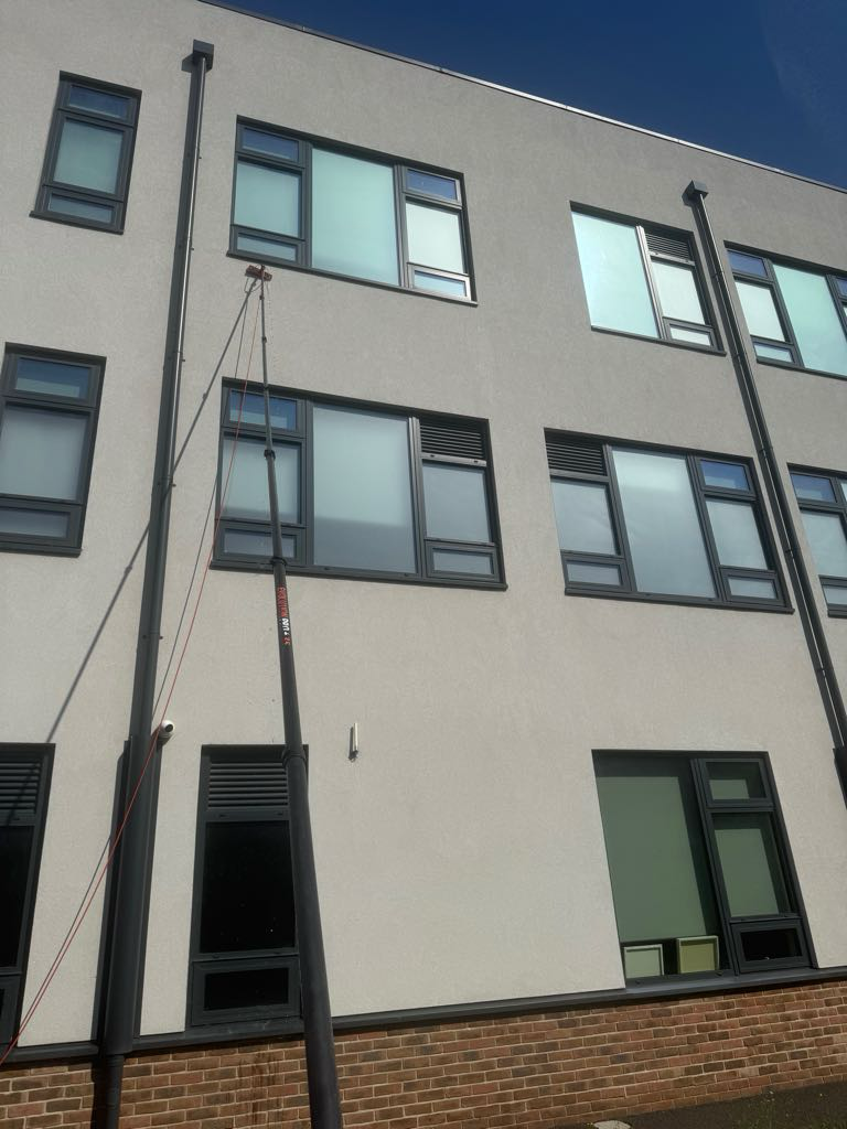 Professional window cleaner using a water-fed pole system to clean the upper-floor windows of a modern commercial building