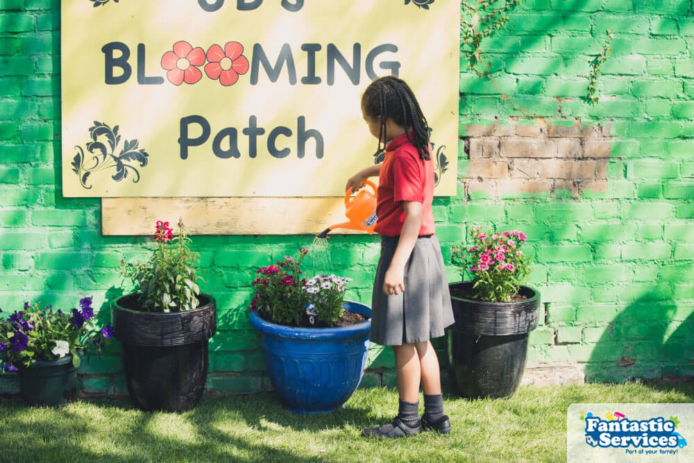 student-watering-plants-blooming-patch-garden