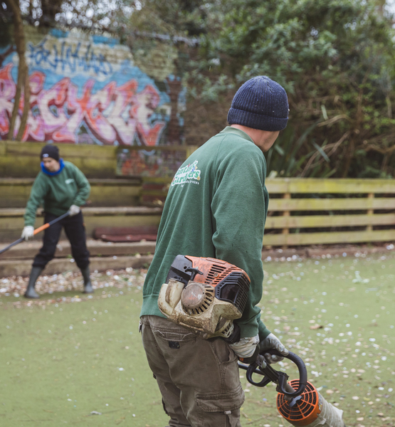 playground-and-garden-maintenance Two gardeners maintaining a children’s outdoor area with trimmers and leaf blowers