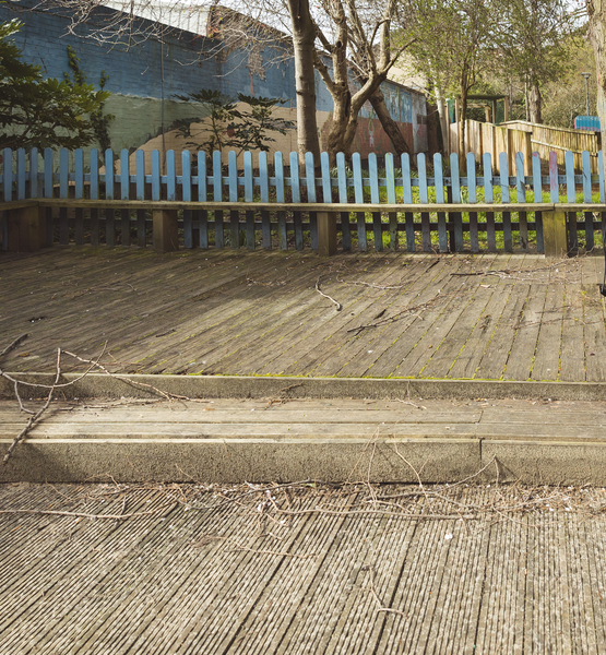 wooden-deck-playground-maintenance Wooden deck area in a children’s outdoor playground with steps and a blue picket fence
