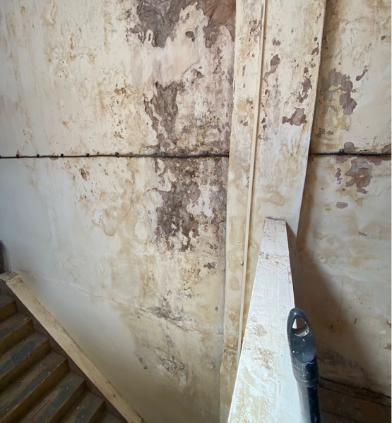 treated-mould-affected-stairwell-wall Stairwell wall after professional mould removal, showing areas of damaged plaster and moisture staining.